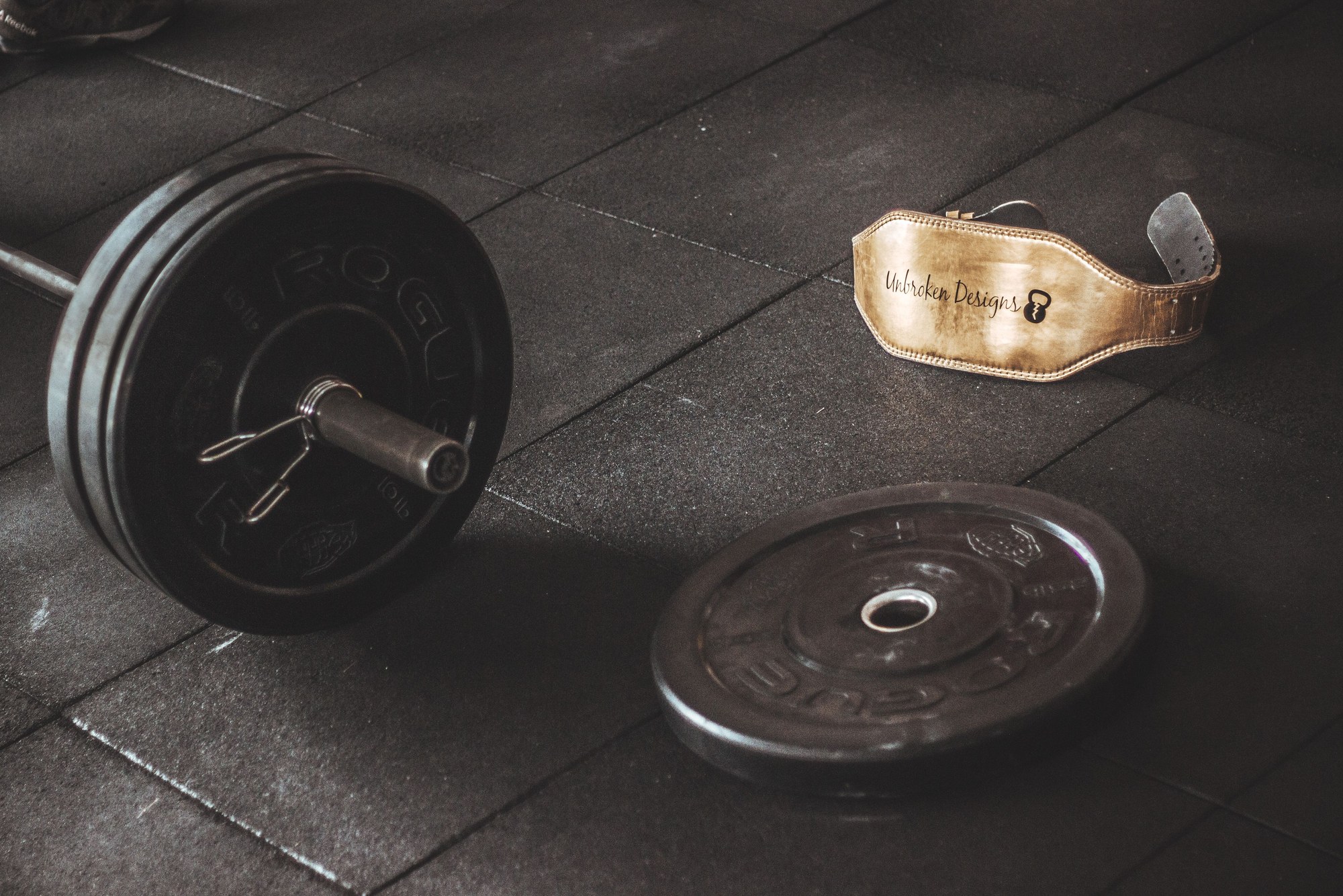 Barra con discos y cinturón de levantamiento en el piso del gimnasio